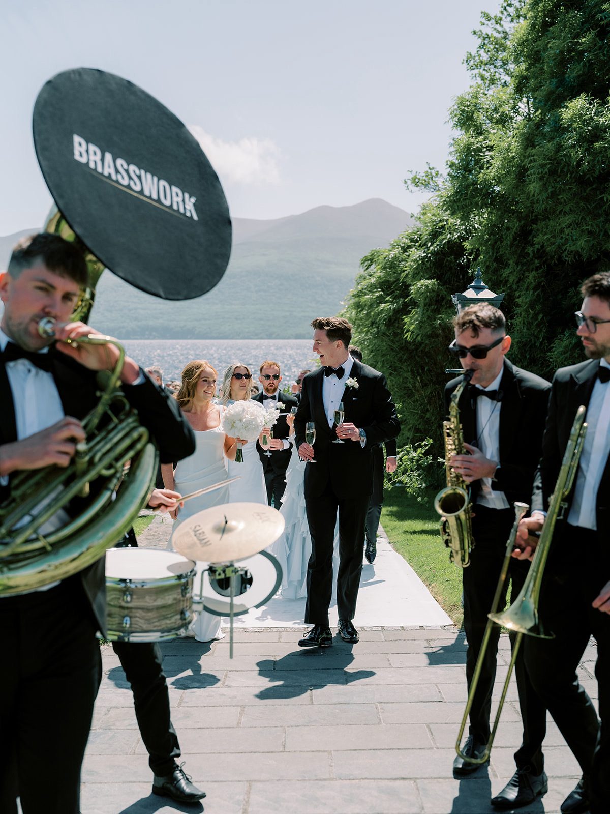 Bride and groom walking through the band with champagne, lake and mountains behind
